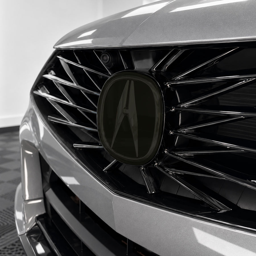 2021–2025 Acura TLX front emblem with smoked tint overlay muting the factory chrome logo