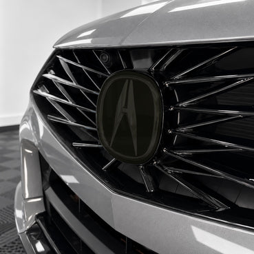 2021–2025 Acura TLX front emblem with smoked tint overlay muting the factory chrome logo
